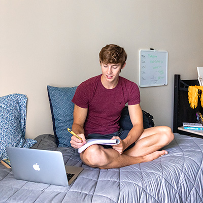 UWM white male student sitting on bed in dorm room and studying